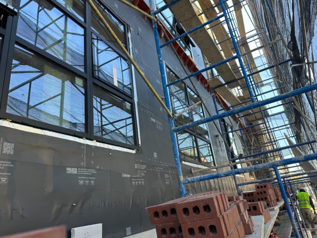 Residential building under construction showing vapor-permeable membrane on exterior walls, surrounded by scaffolding.