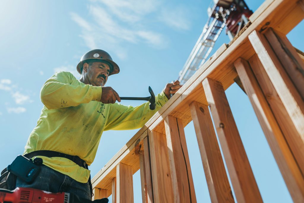 A contractor works on a wall frame under a blue sky.