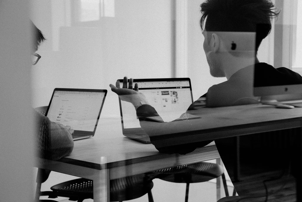 Two people work at a table with laptops in front of them.